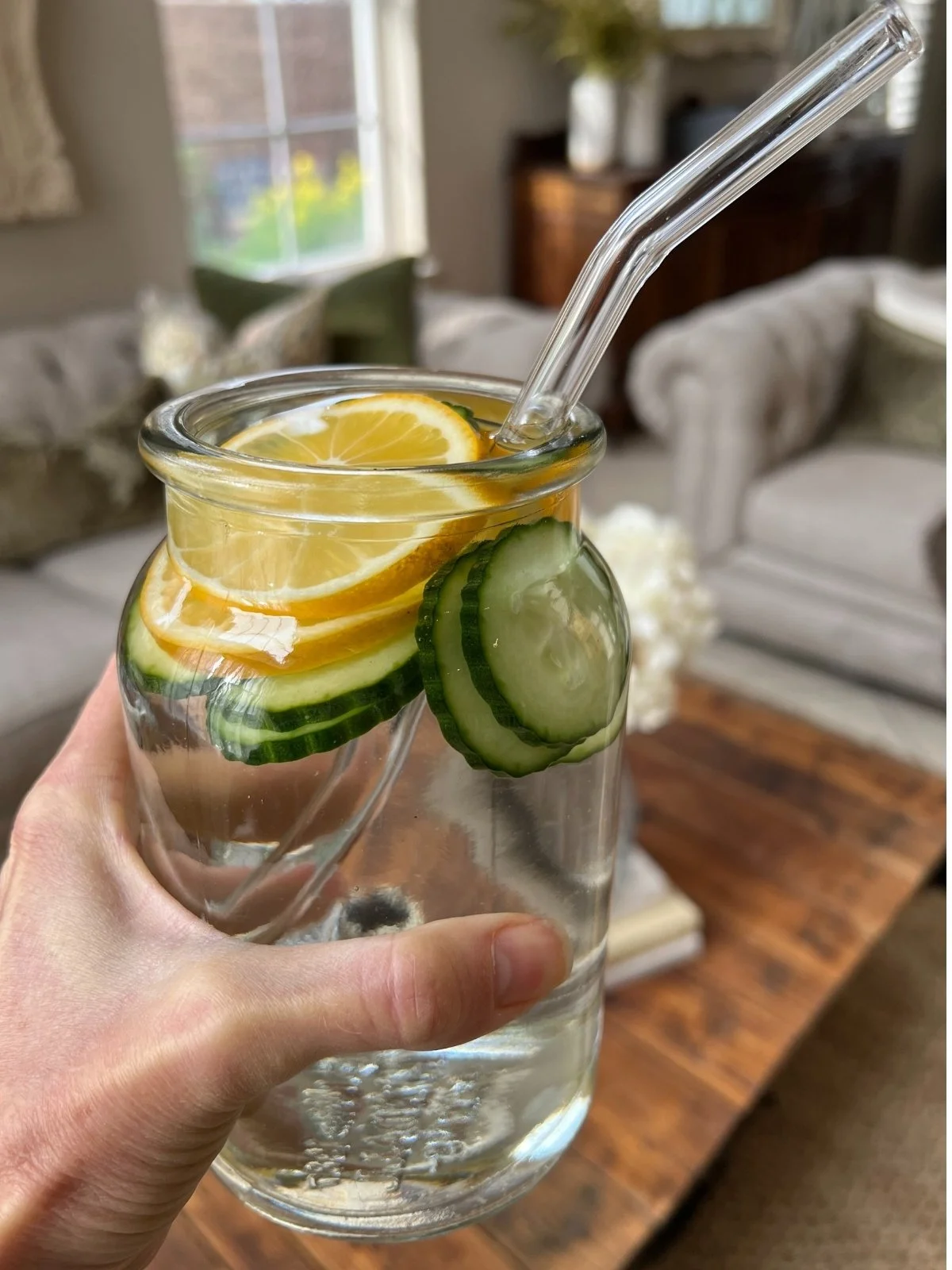 Glass jar of water with lemon and cucumber sliced held by hand