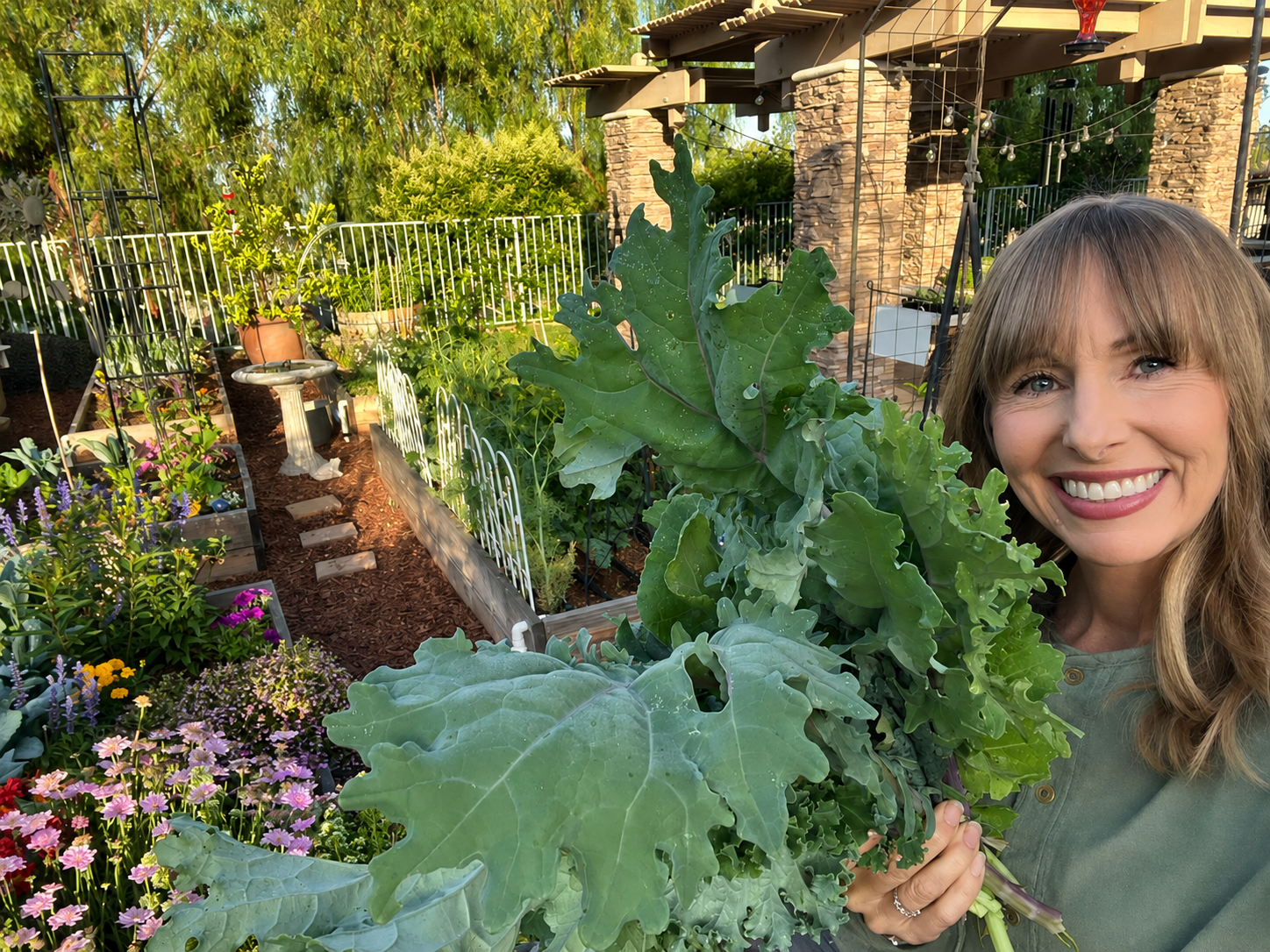 Michelle in her home garden surrounded by leafy greens and flowering plants
