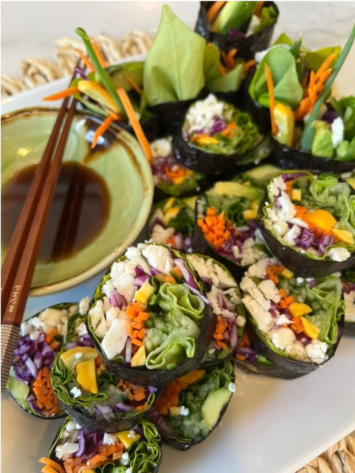 Colorful raw vegan sushi rolls filled with leafy greens, cabbage, carrots, avocado, and other vegetables served with a dipping sauce.