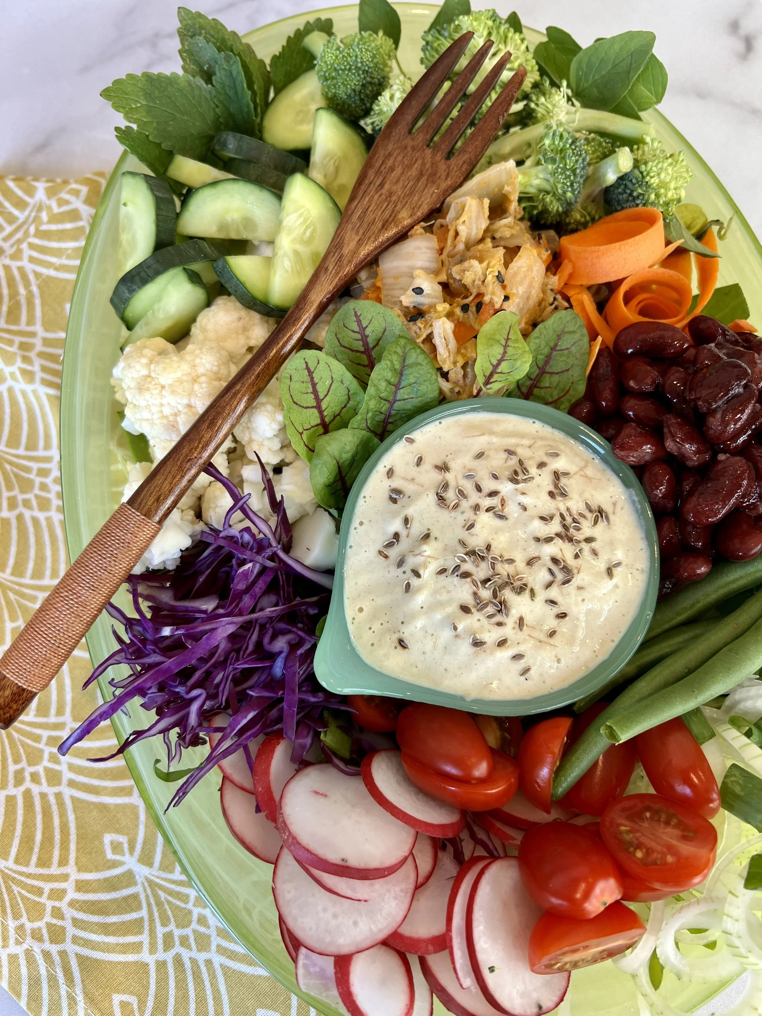 Colorful whole-food plant-based platter with beans, cabbage,radishes, carrots, broccoli, cucumber, tomatoes, and a creamy dressing