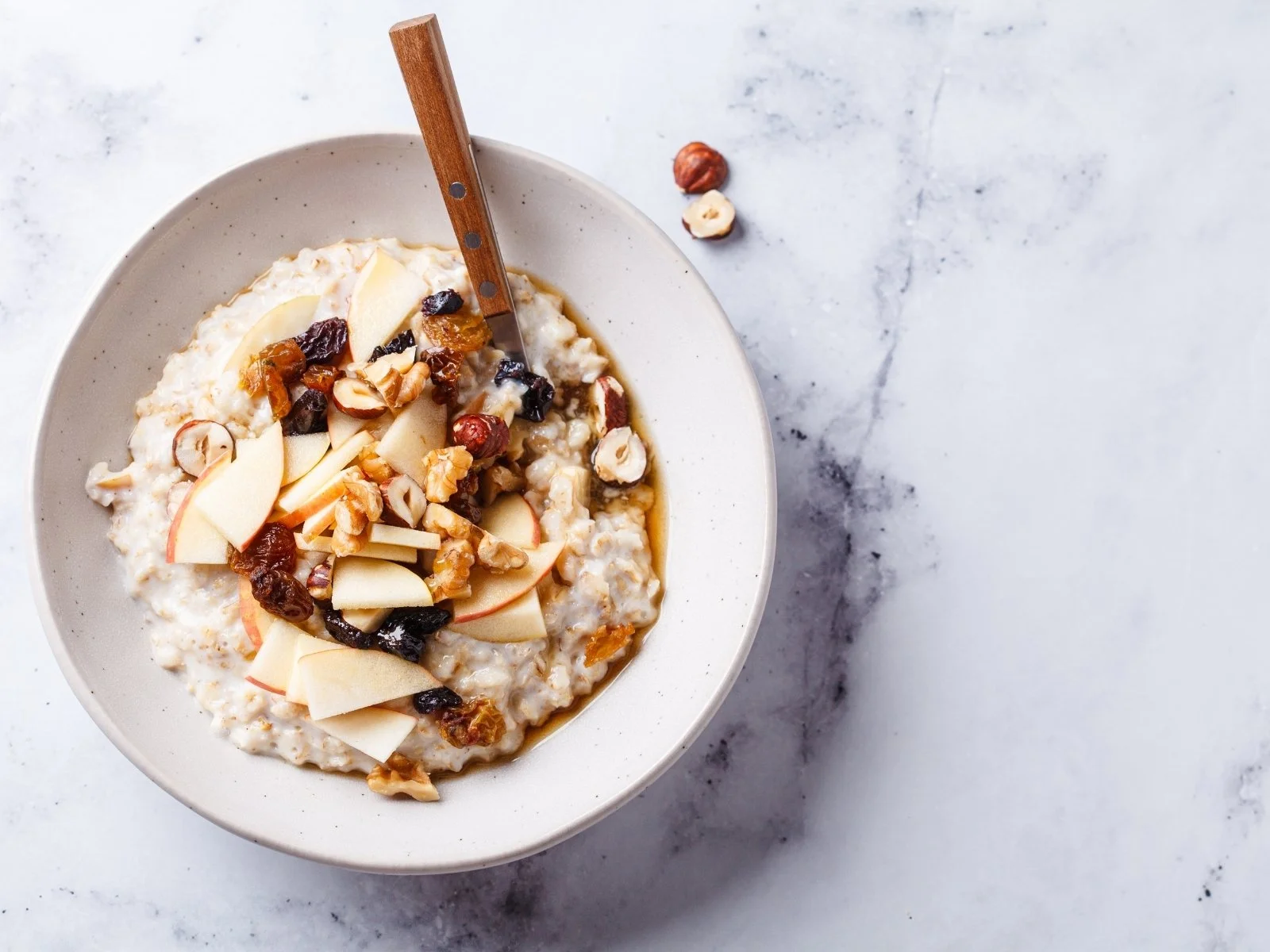 Bowl of oatmeal topped with sliced apple, nuts, and dried fruit.