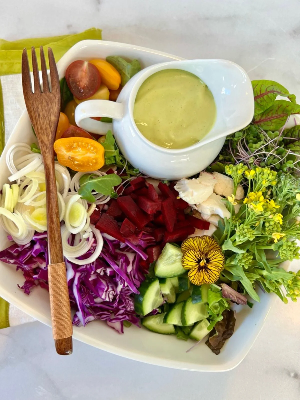 Colorful raw vegan salad with cabbage, beets, cucumber, greens, sprouts, and cauliflower served with creamy avocado dressing.