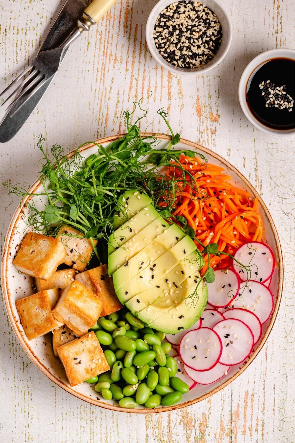 Plant-based bowl with tofu, edamame, avocado, radishes, carrots, and greens