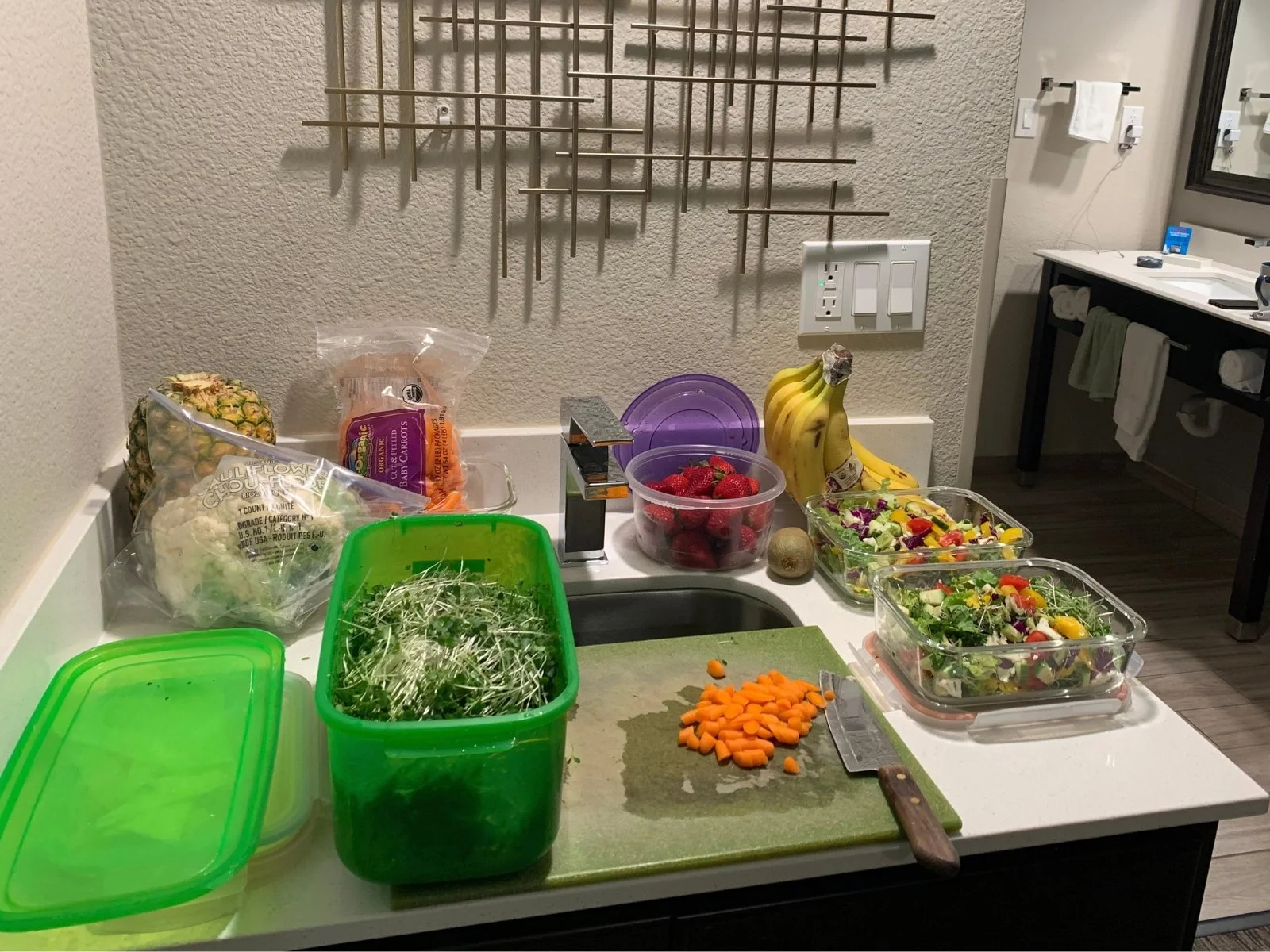 Fruit, vegetables, and salads set up for GAIP food preparation in a hotel room.
