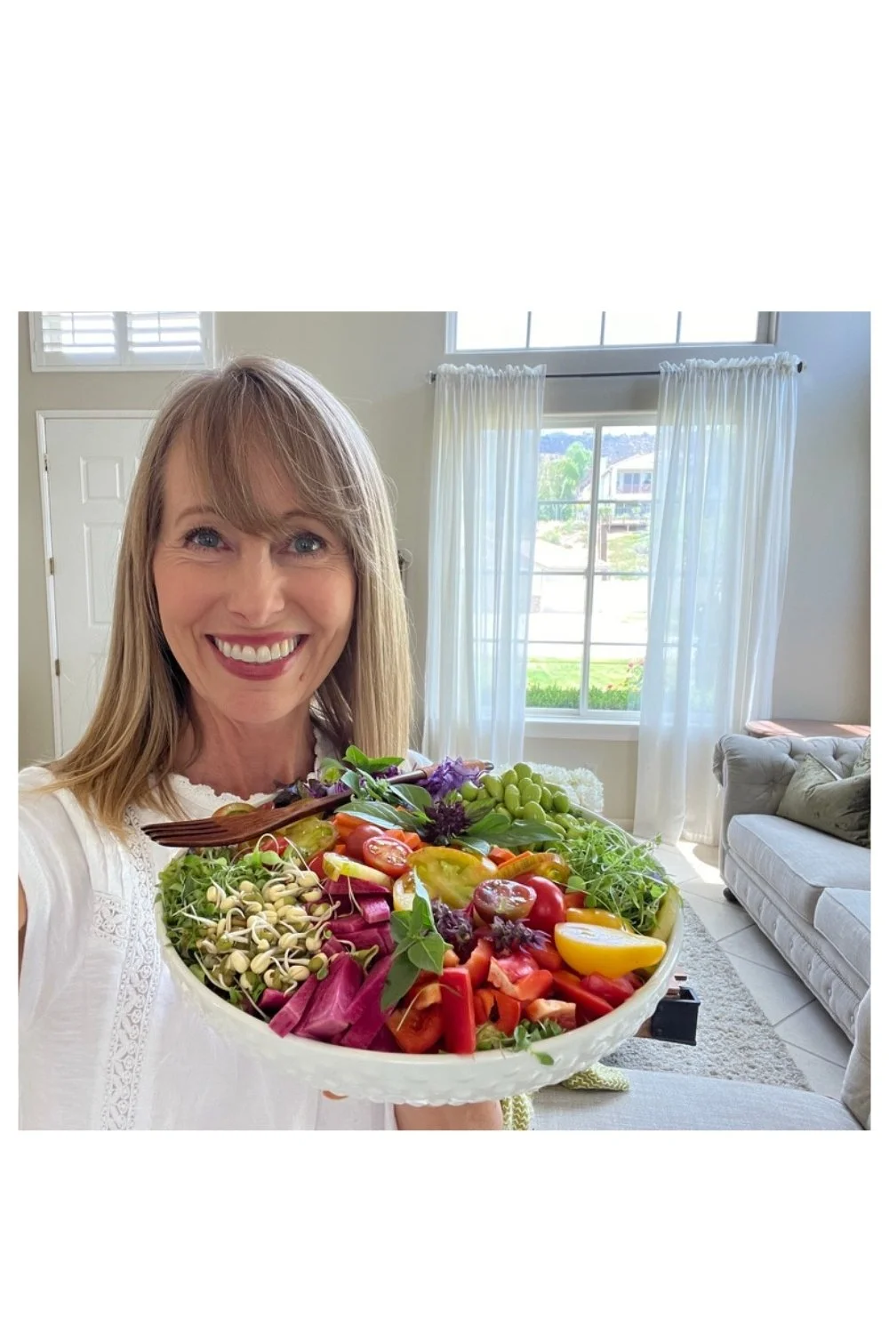 Woman holding a large colorful salad filled with vegetables, greens and sprouts