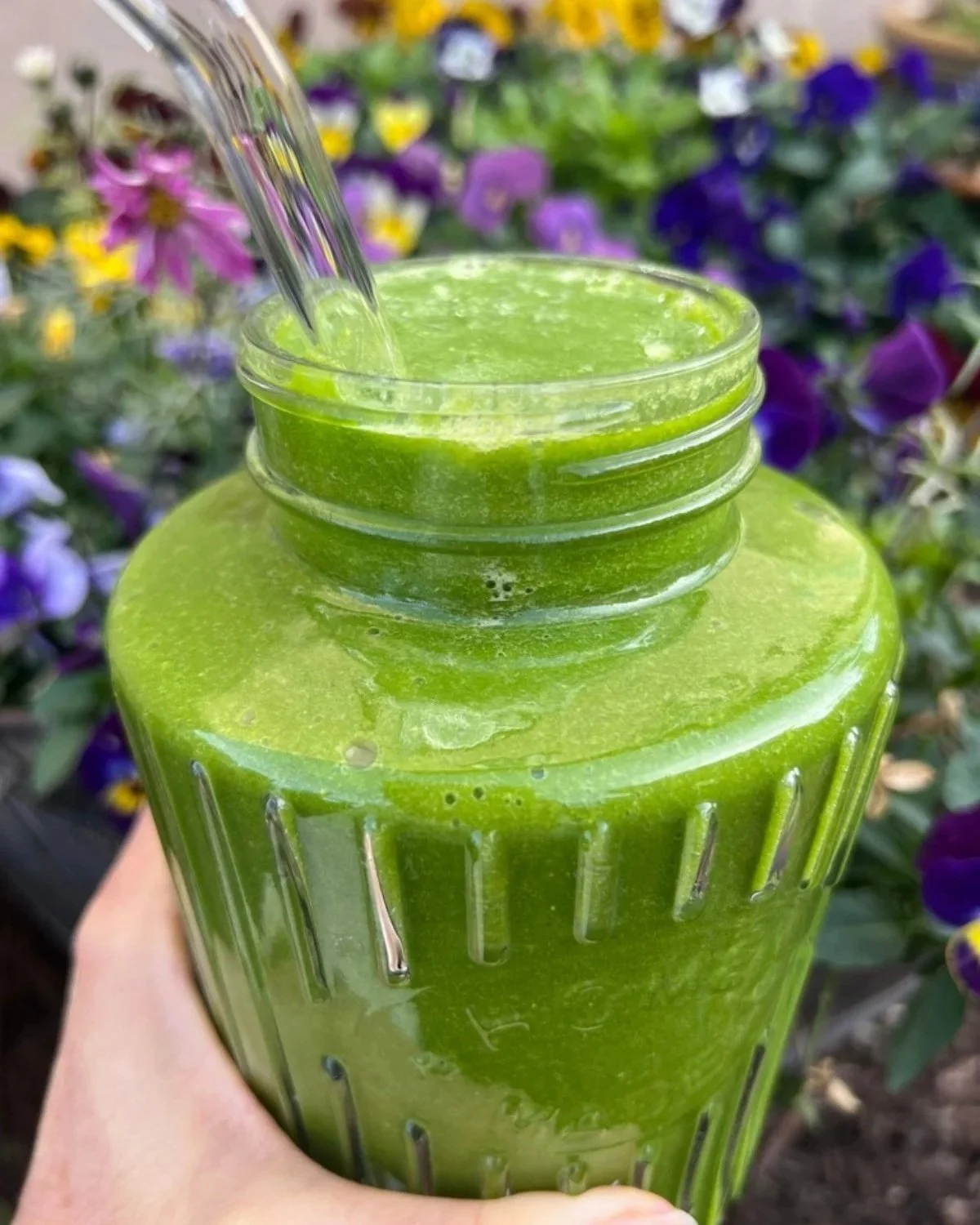 Bright green hyper-nourishing smoothie in a glass jar held outside.