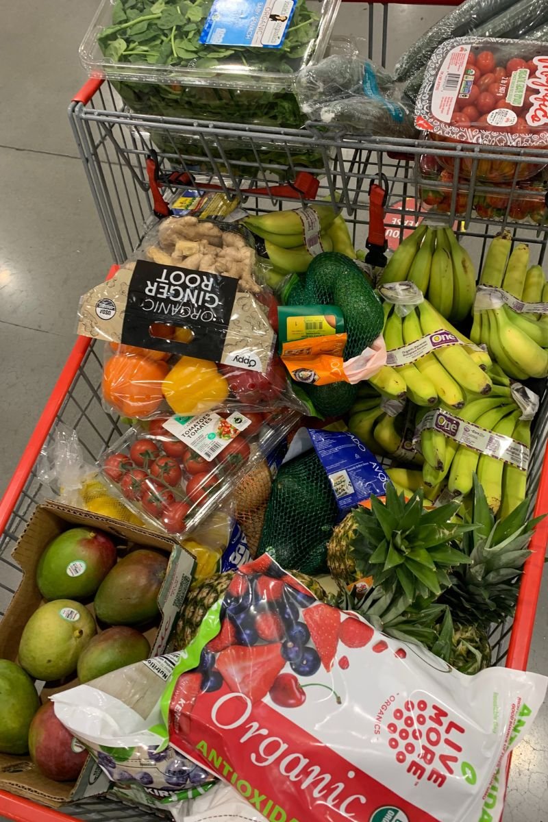 Shopping cart filled with bananas, mangoes, berries, avocados, greens, and other produce for a hyper-nourishing plant-based diet.