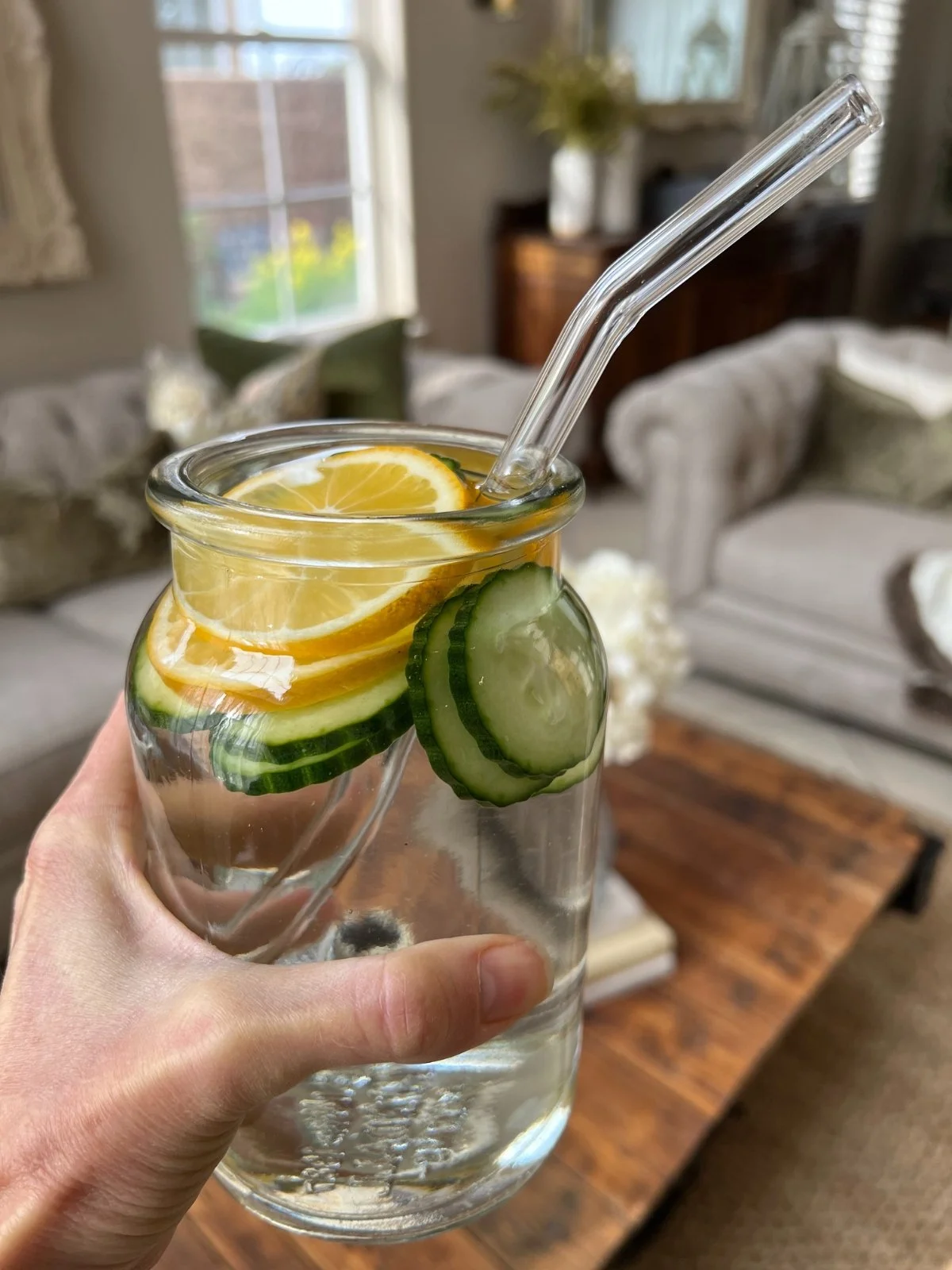 Lemon and cucumber slices in water in a glass jar with glass straw.