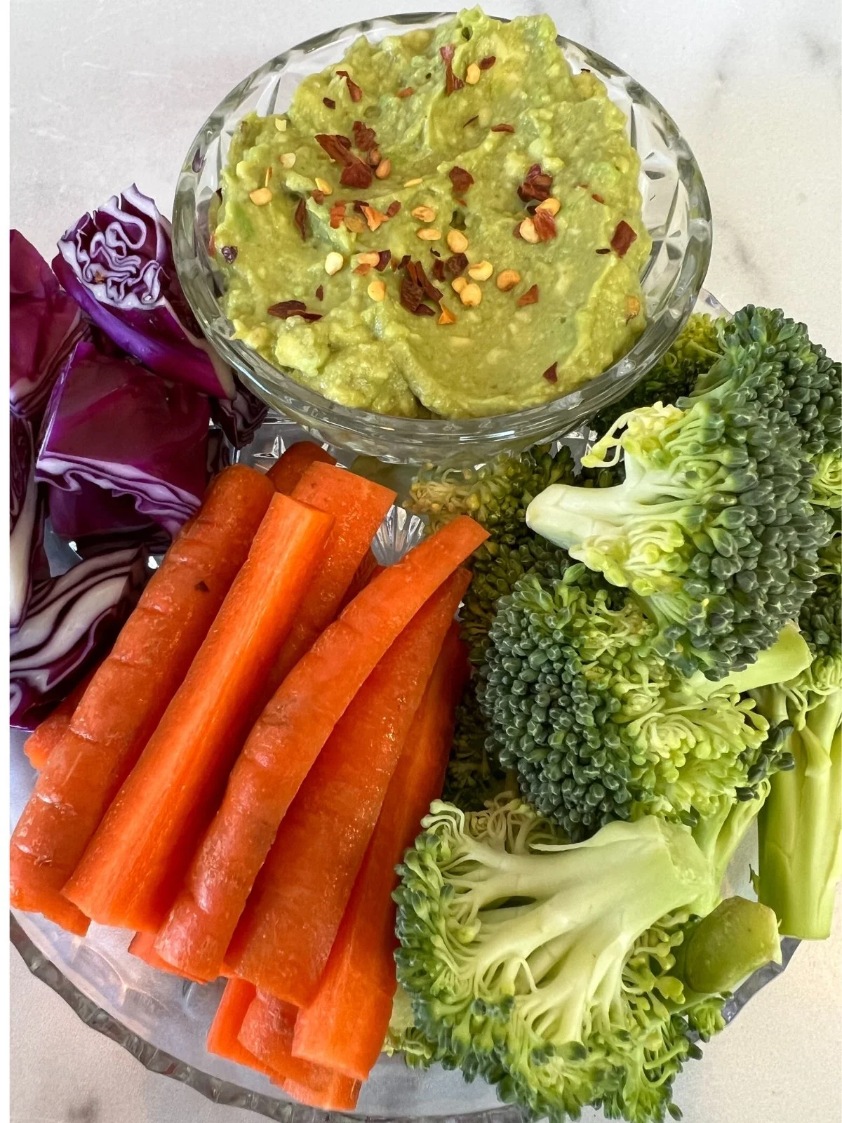 Raw broccoli, red cabbage, and carrots served with homemade guacamole for an easy plant-based meal.