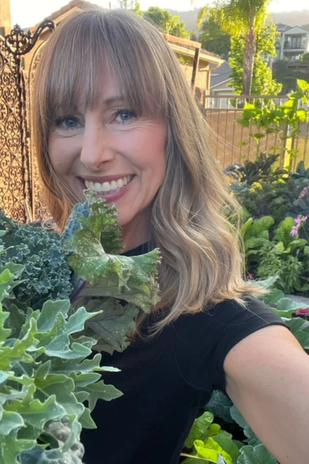 Michelle holding frshly harvested greens in a backyard vegetable garden