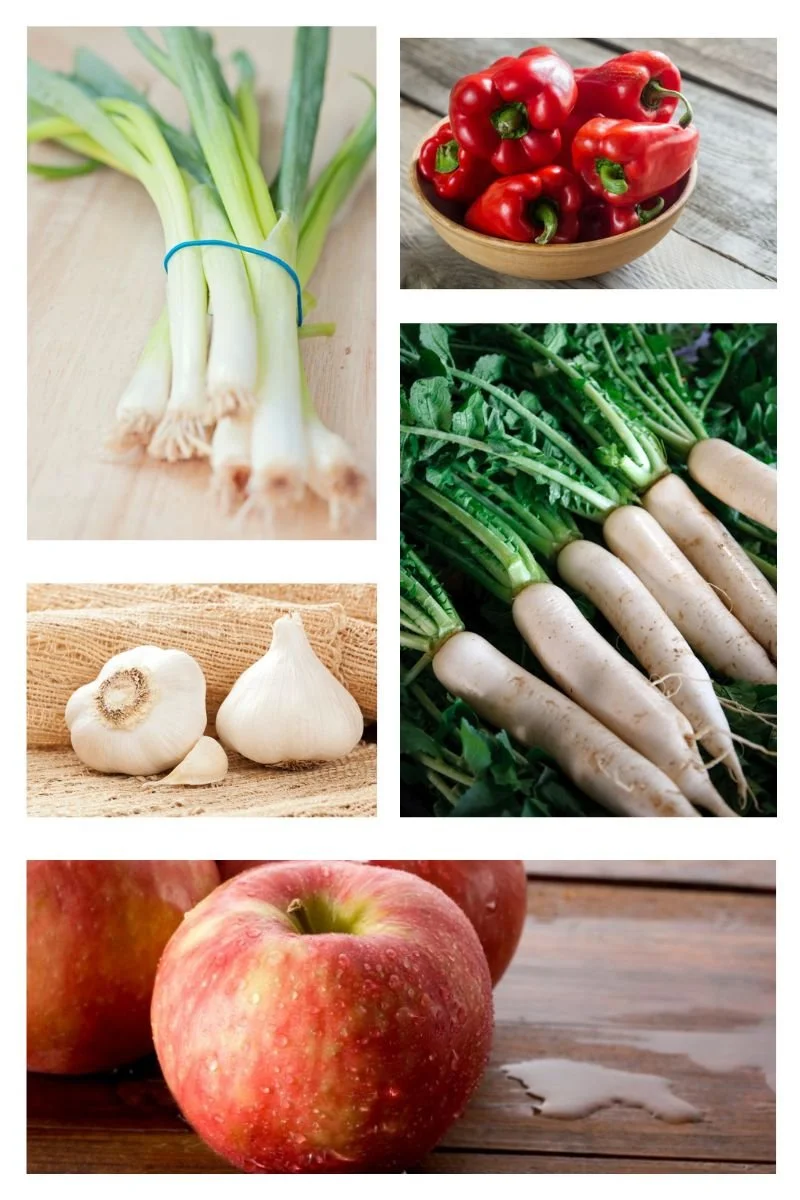Fresh ingredients for homemade raw vegan kimchi including green onions, red bell peppers, daikon radishes, garlic, and apples.
