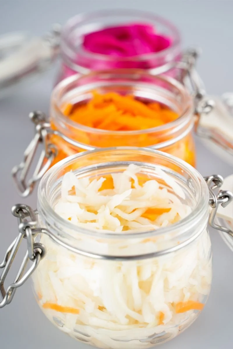 Homemade fermented sauerkraut and carrots in small glass jars.
