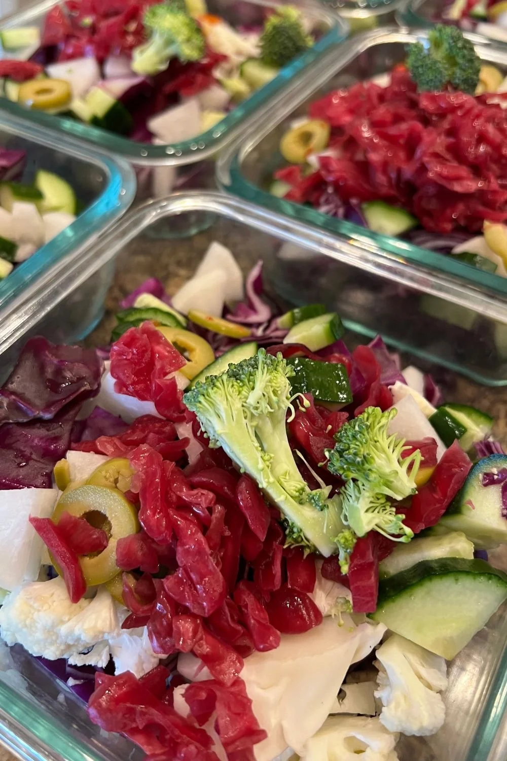 Meal-prep containers filled with raw vegetables, broccoli, cucumber, cabbage, and sauerkraut