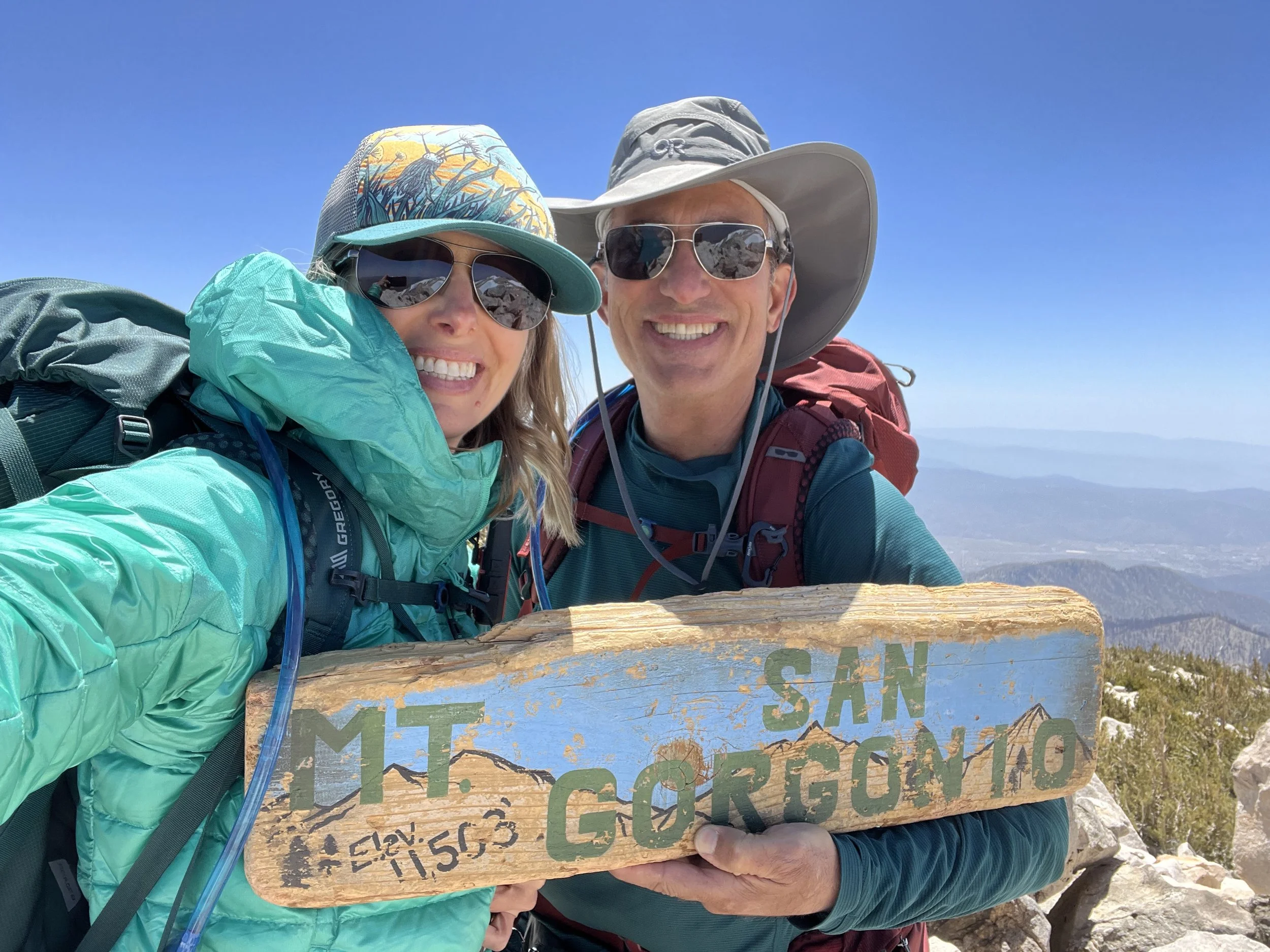 Michelle and her husband smiling at the summit of Mt. San Gorgonio, the highest peak in Southern California, during a backpacking adventure.