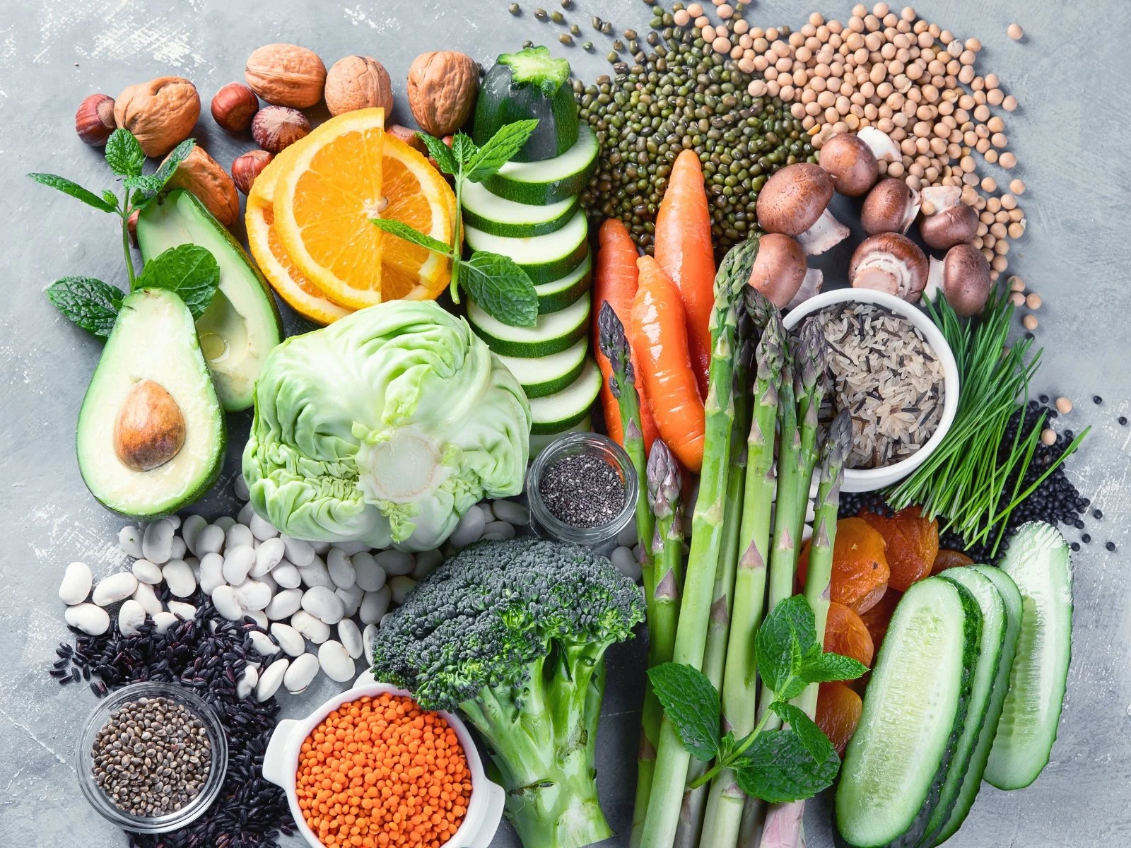 Colorful assortment of whole plant foods including vegetables, legumes, seeds, nuts, whole grains, and fruit