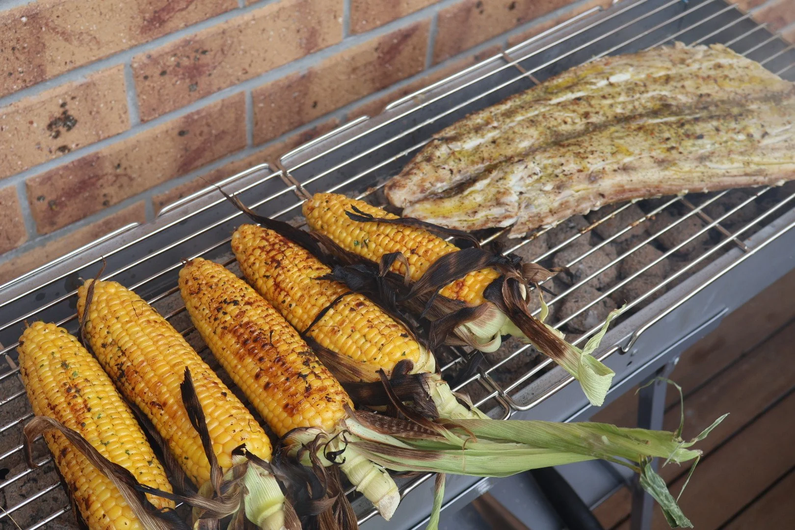 Corn on the cob and a rack of ribs being grilled over an outdoor barbecue
