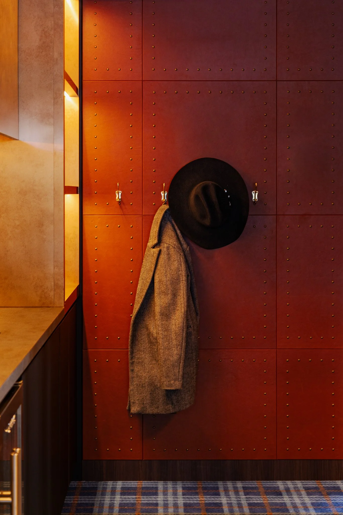 A tweed coat hanging on a aeather panelled wall with rivets at a private suite, Allianz Stadium