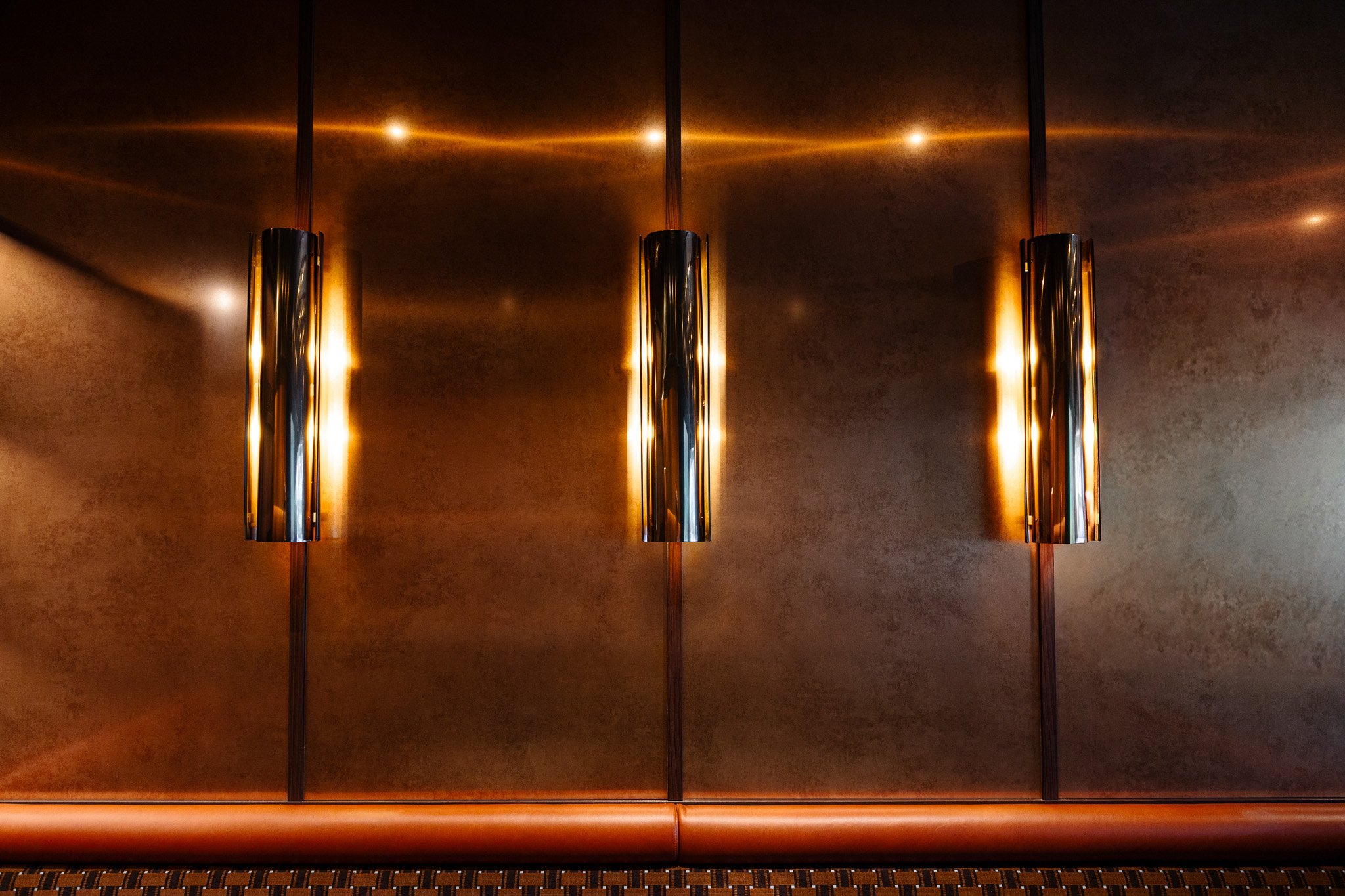 detail of a wall at a stadium suite, metallic cylinder lights against brushed brass panelled with upholstered booth seat