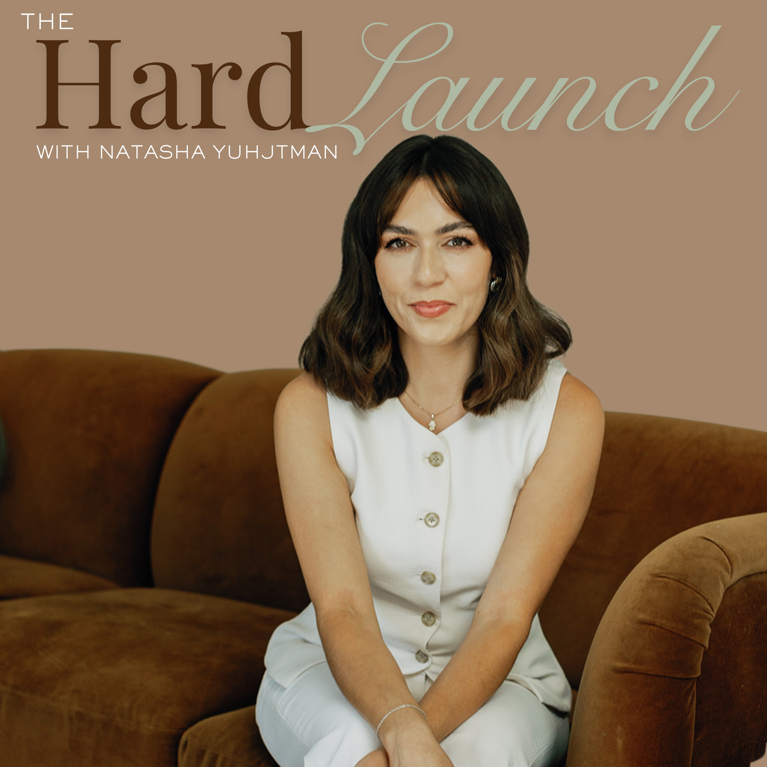 A woman with shoulder-length brunette hair, wearing a white sleeveless dress, sitting on a brown sofa with a smiling expression.