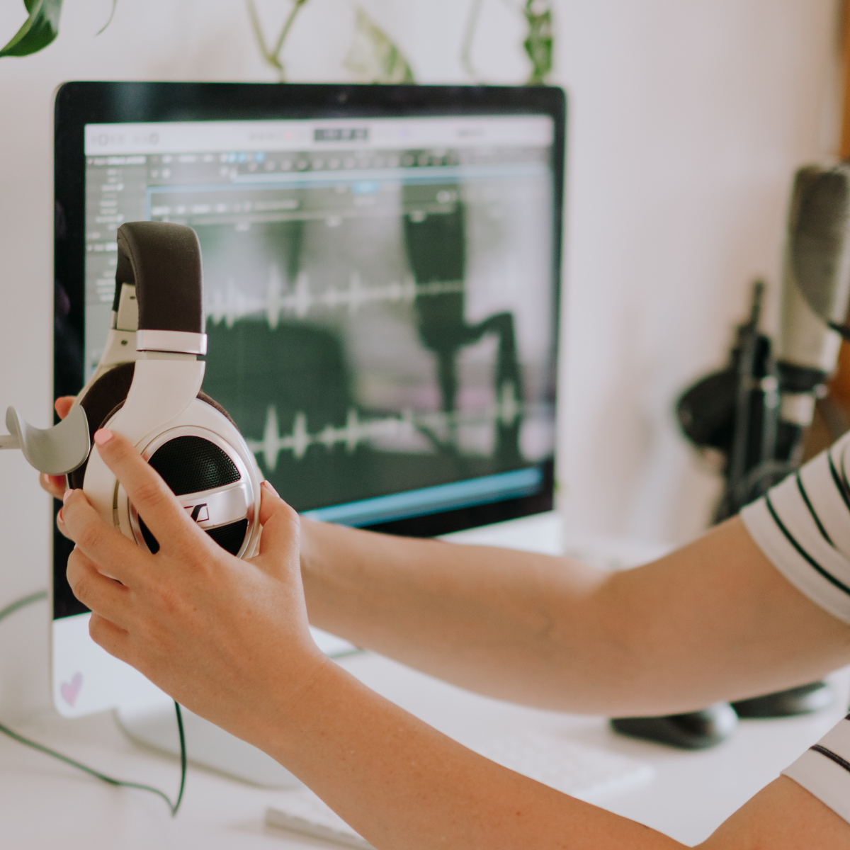 Person holding white and brown headphones in front of computer monitor displaying audio editing software