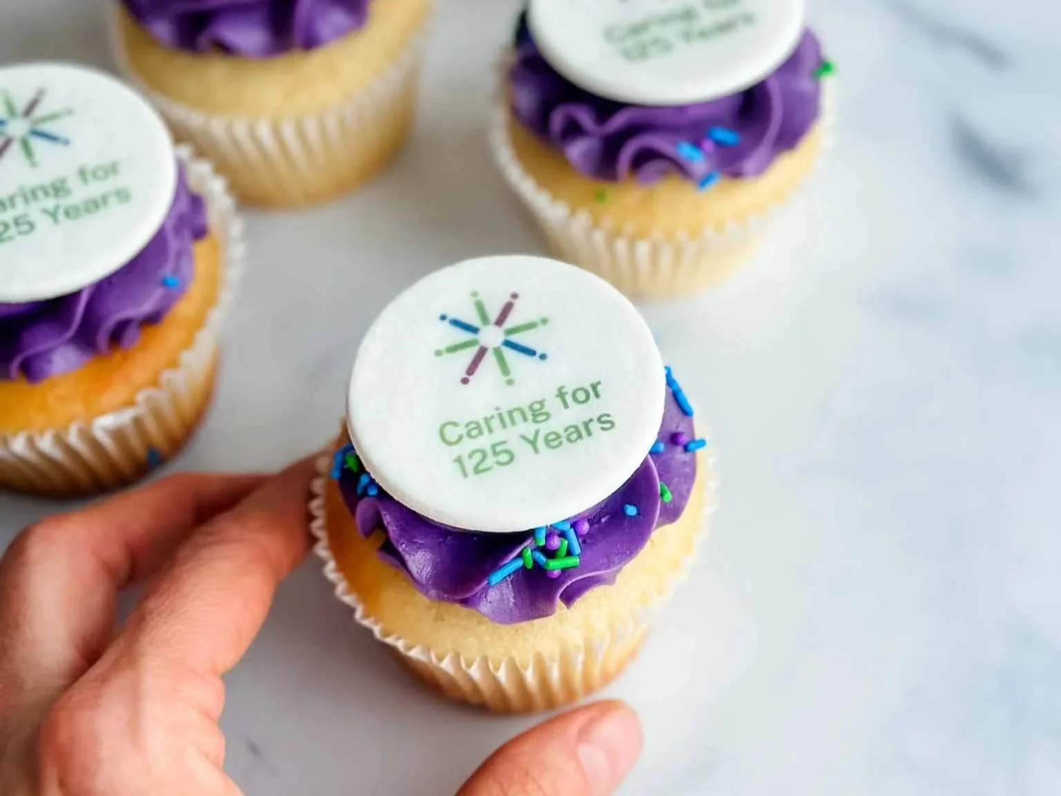 hand reaching for purple cupcakes with 125 anniversary personalization
