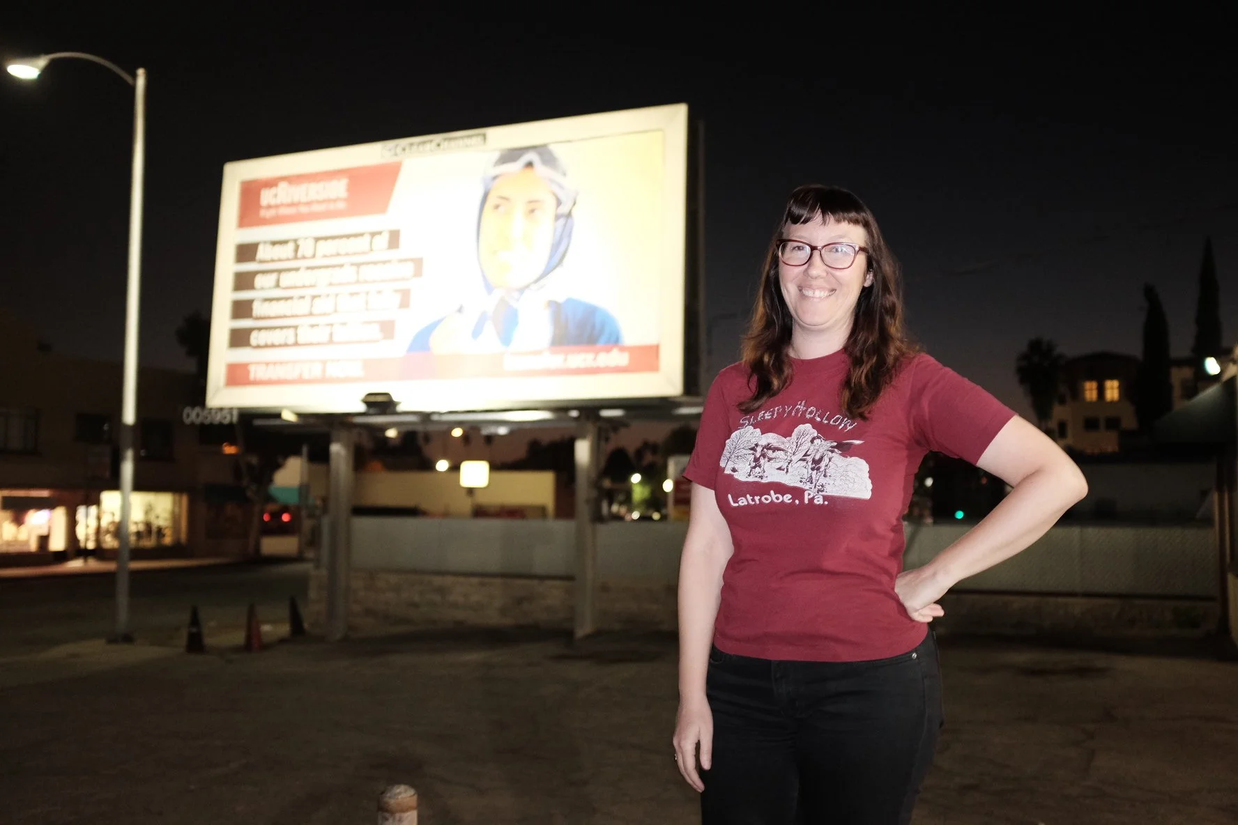 A woman stands in front of a billboard she wrote.