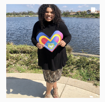  A person holds a paper heart. They are standing near the waterfront. 