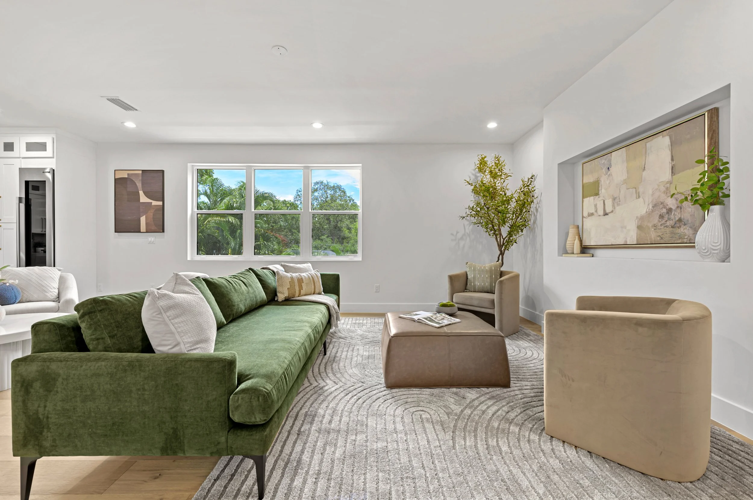Living room with green sofa, beige armchairs, a window, a patterned rug, and modern decor.