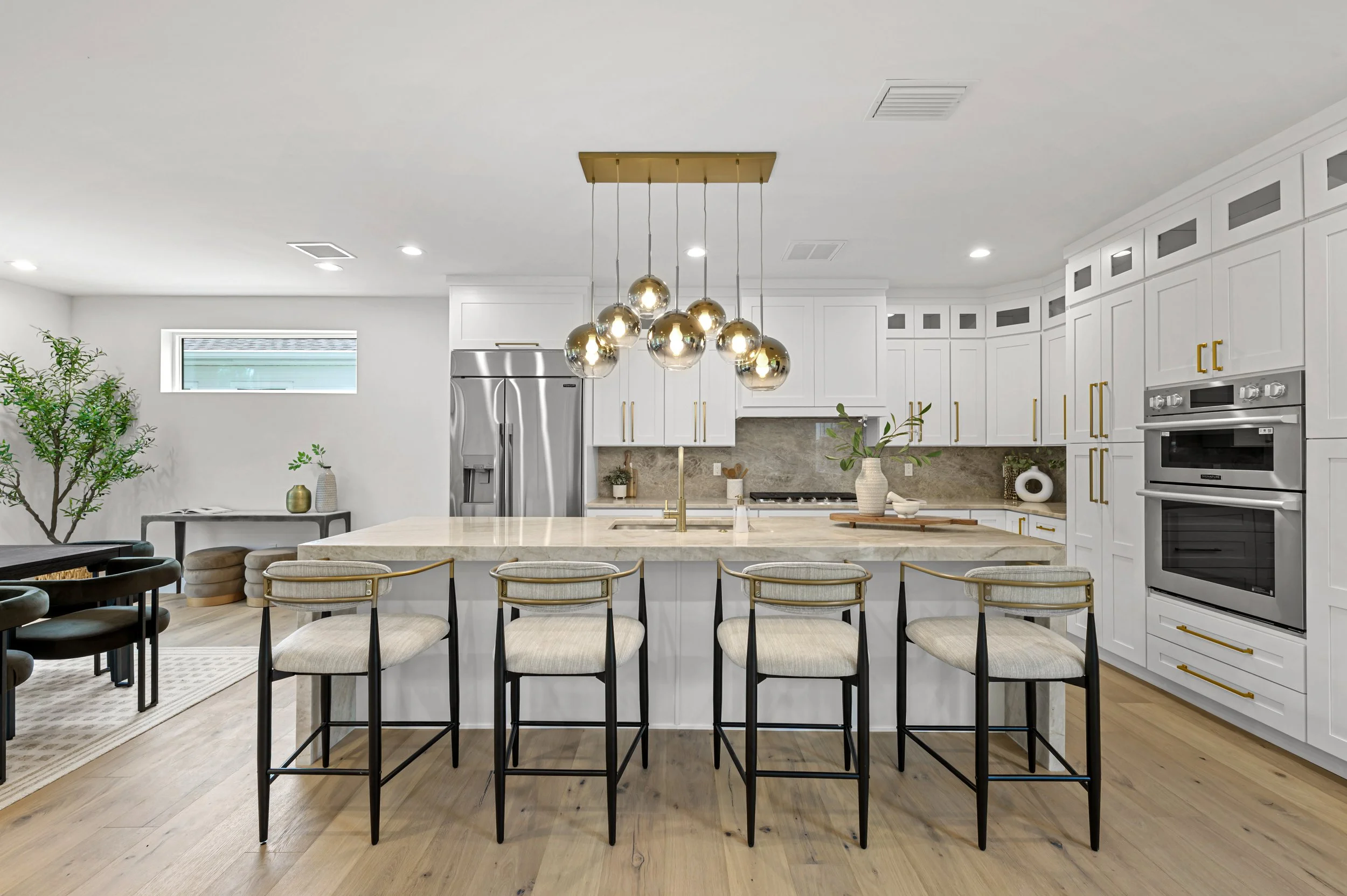 Modern kitchen with white cabinets, marble island, stainless steel appliances, and a gold chandelier above the island.