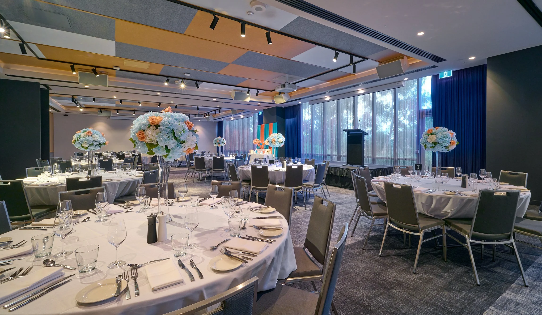 Elegant banquet hall with round tables set for an event, featuring flower centerpieces, white tablecloths, and glasses.