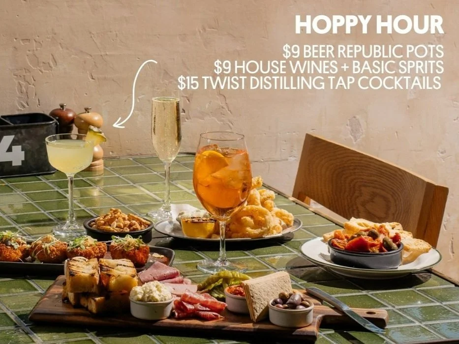 An assorted spread of appetizers and drinks on a tiled table for Hoppy Hour, with offers on beer, wine, and cocktails.