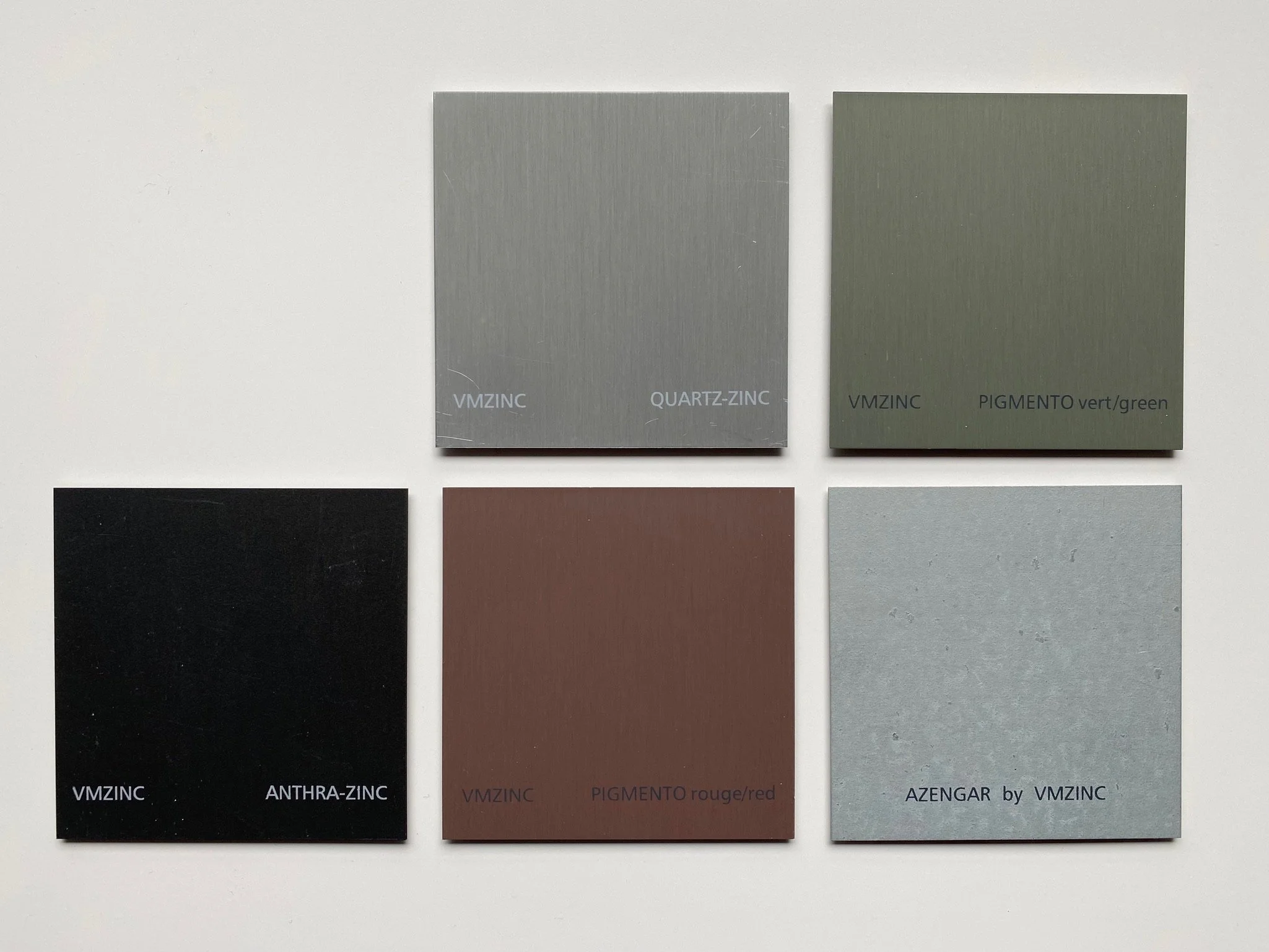 Échantillons de couleurs VMZINC affichant cinq tons différents de zinc, incluant QUARTZ-ZINC, PIGMENTO vert, ANTHRA-ZINC, PIGMENTO rouge et AZENGAR.