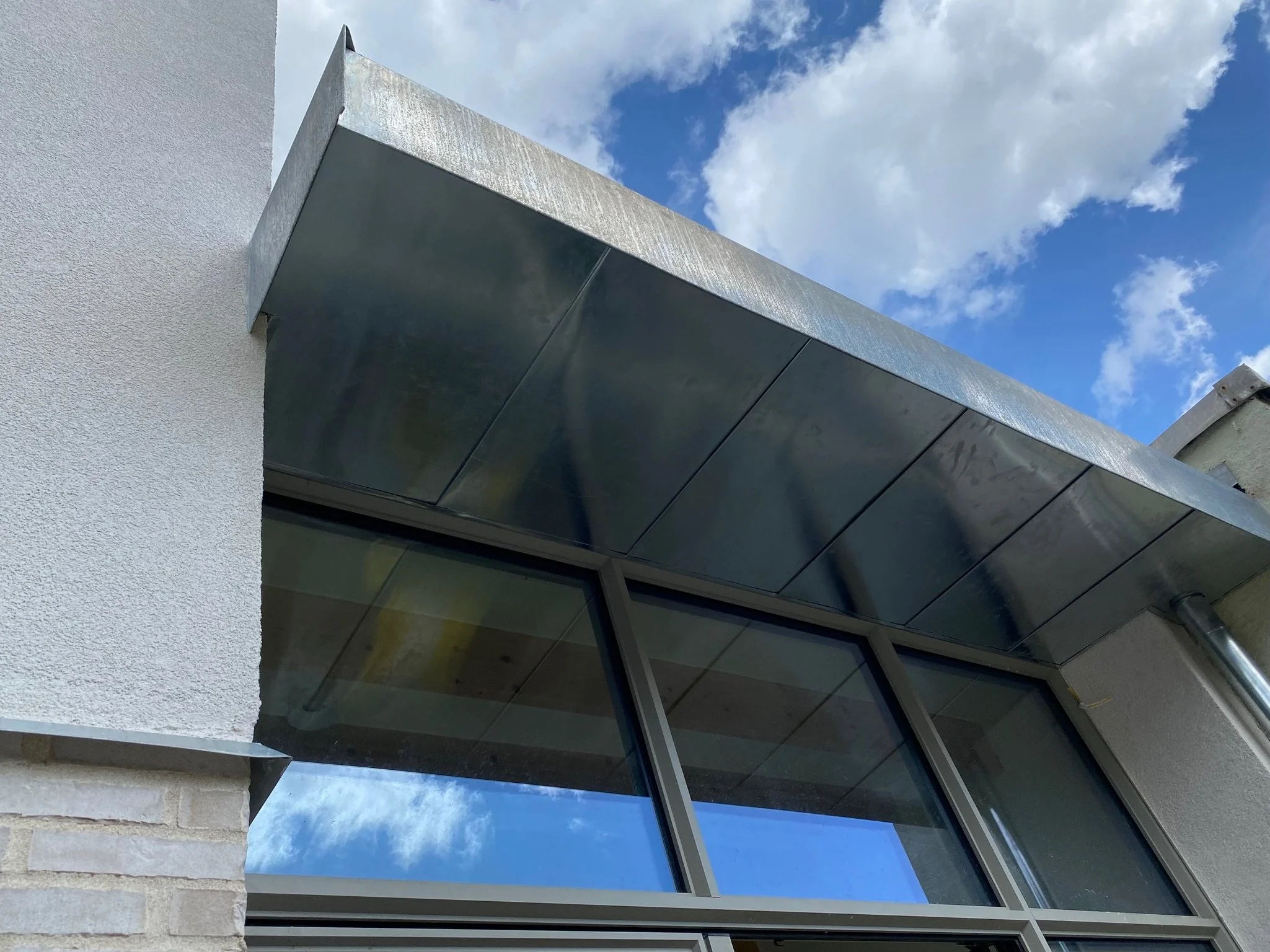 Vue en contre-plongée d'un bâtiment avec des fenêtres en verre et un toit en métal, ciel bleu avec des nuages.