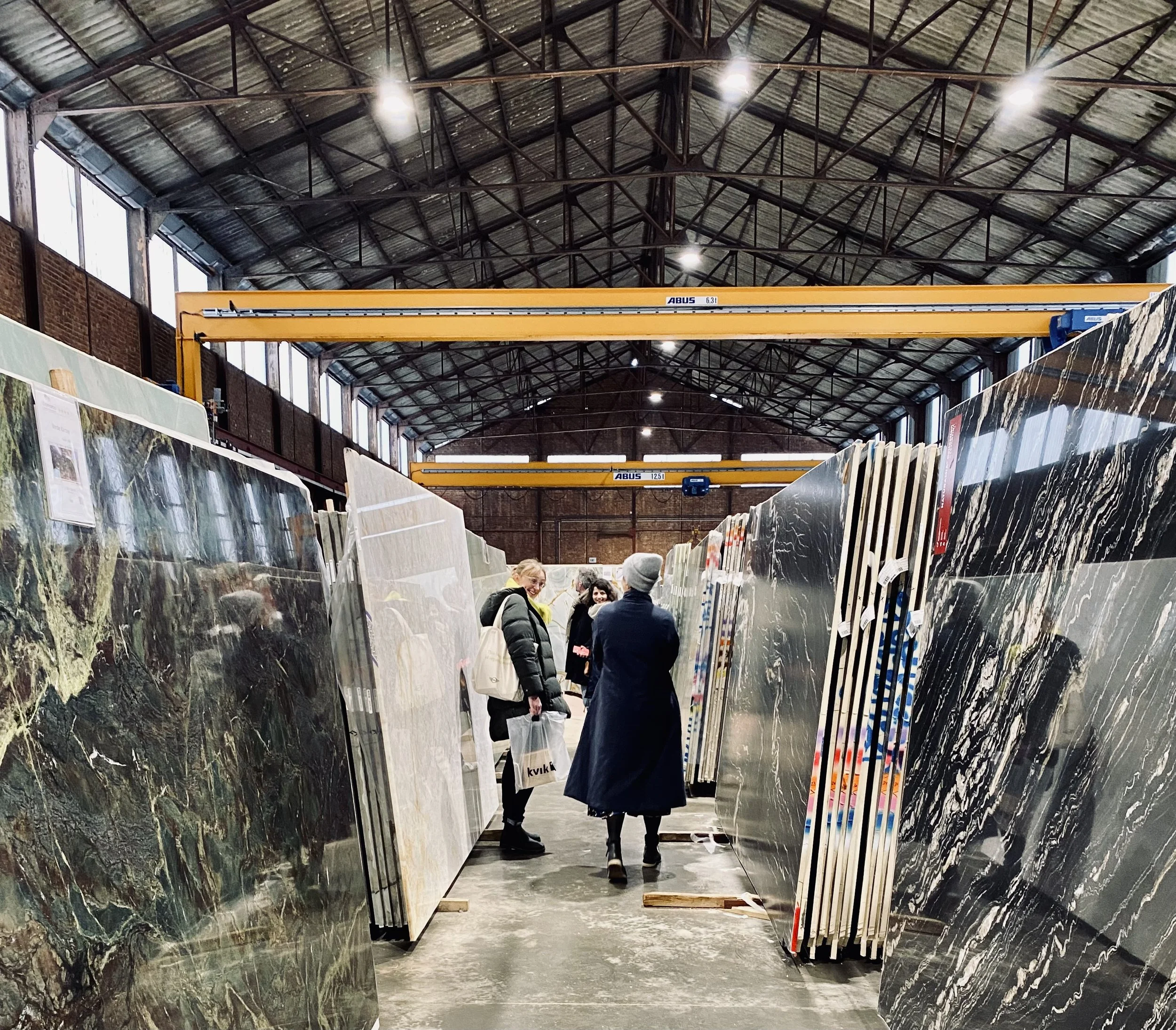 Personnes dans un entrepôt de plaques de marbre ou de granit, examinant des dalles de pierre massive.