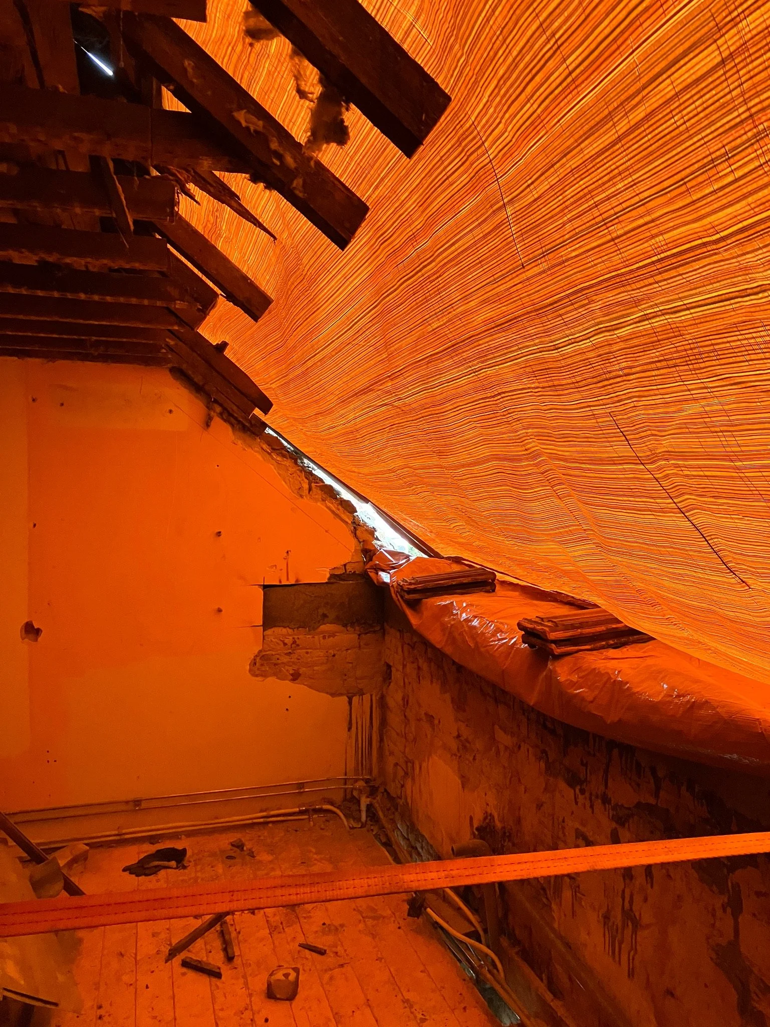 Un grenier en rénovation avec des murs en briques exposées et un toit partiellement recouvert de bâches oranges.