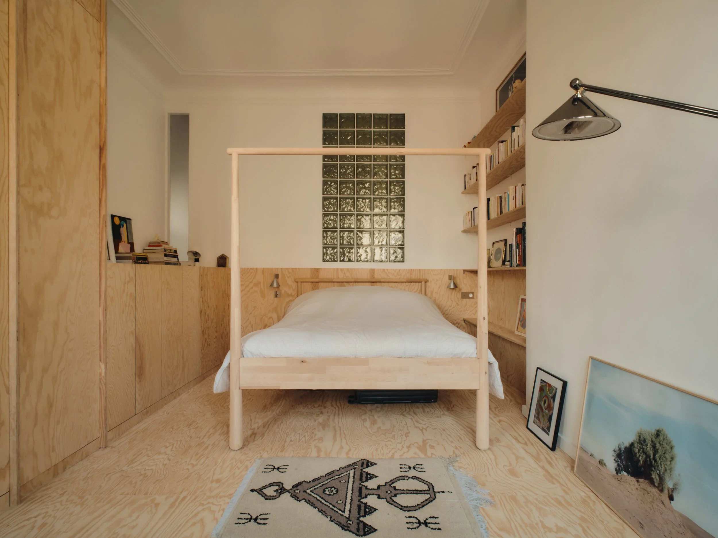 Chambre simple avec lit en bois, étagères de livres, œuvres d'art et parquet en bois natural.