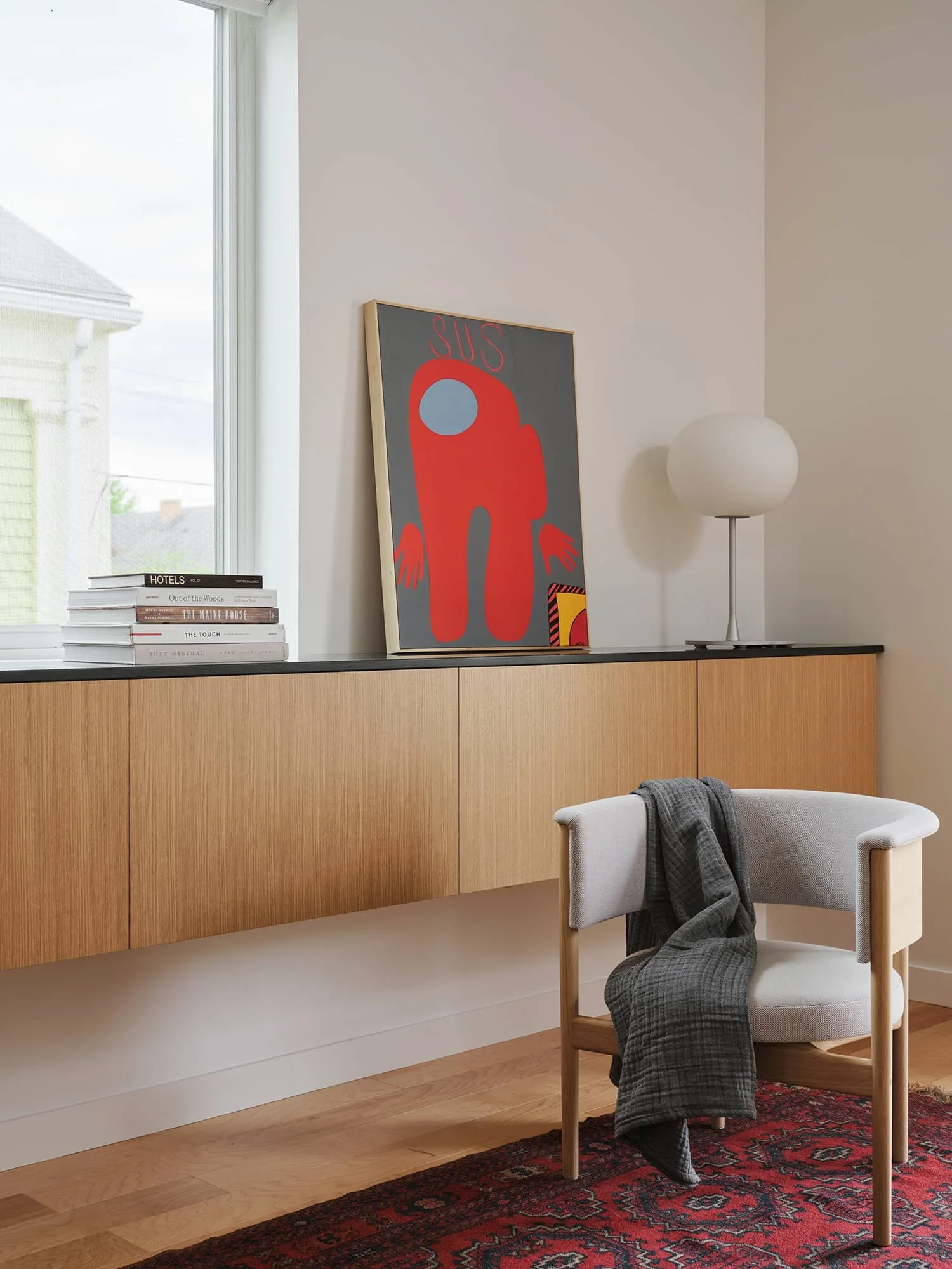 Floating wooden sideboard with black countertop, modern abstract art, lamp and chair.
