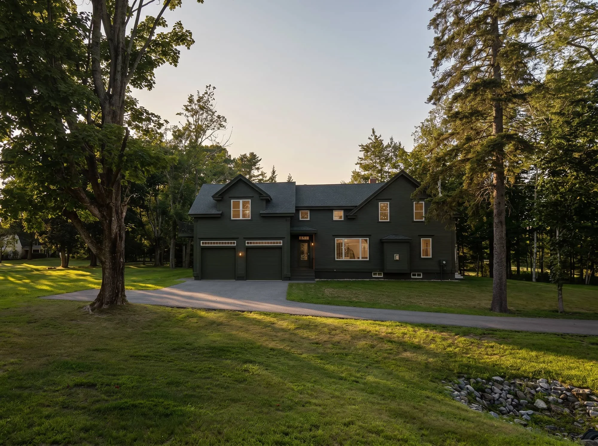 House with dark green siding sitting amongst trees and grass