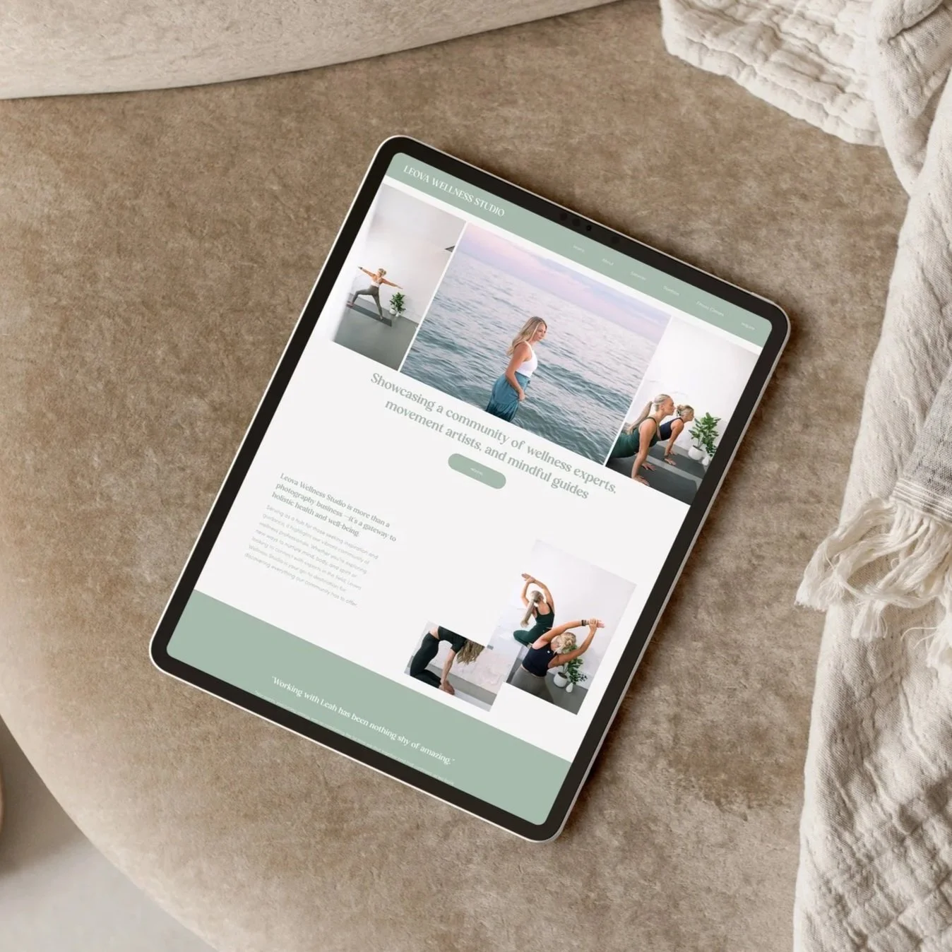 Tablet displaying the Leona Wellness Studio website with images of women practicing yoga and meditation, set on a beige textured surface next to a cream-colored fabric.