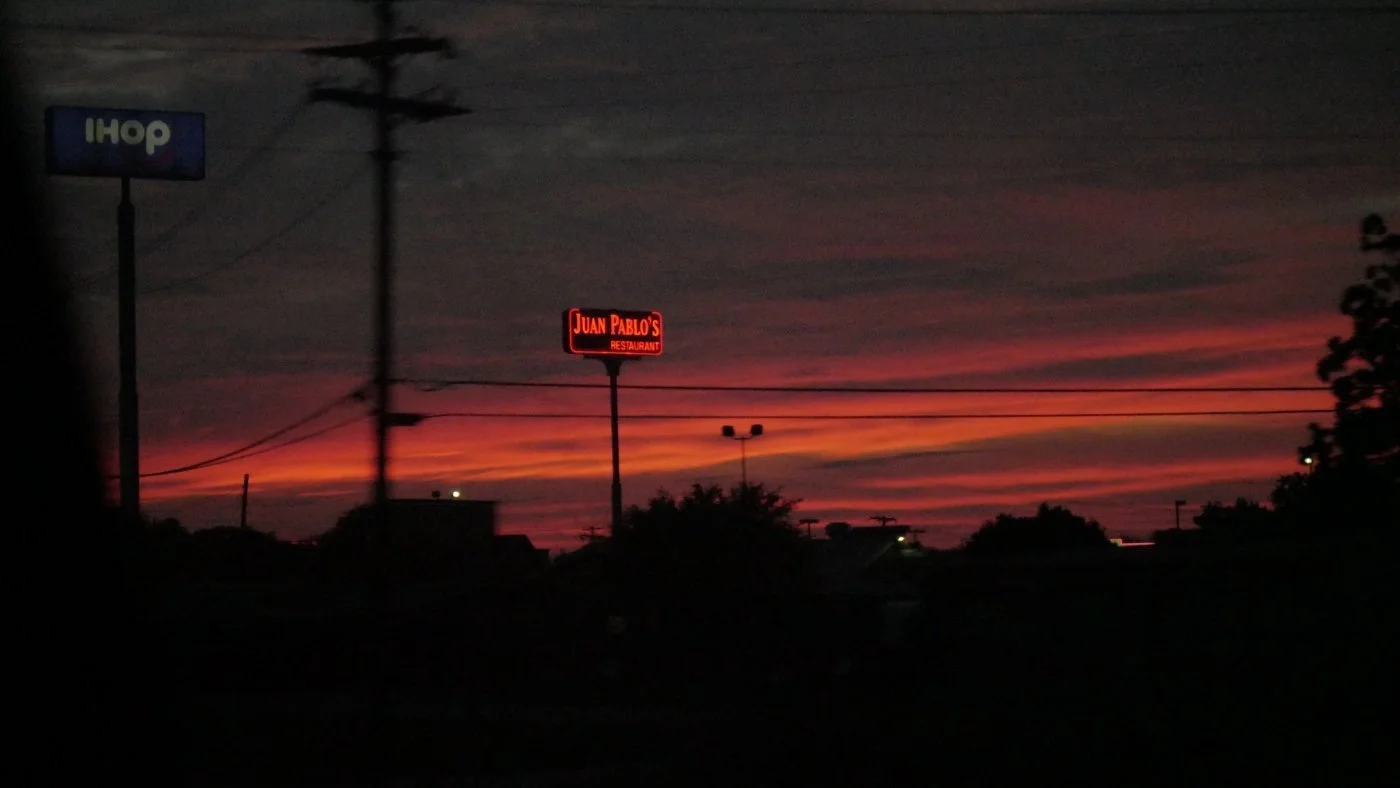 A neon sign under a red sun set.