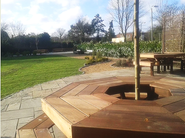 View of a backyard with a wooden deck and outdoor seating area, green lawn, trees, and a clear blue sky.