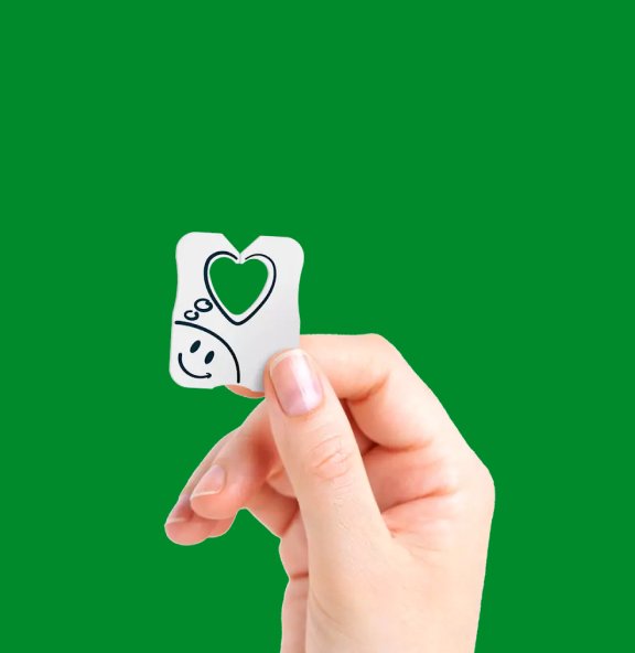 A hand is holding a paper seal with a smiley face on it. The background is green.
