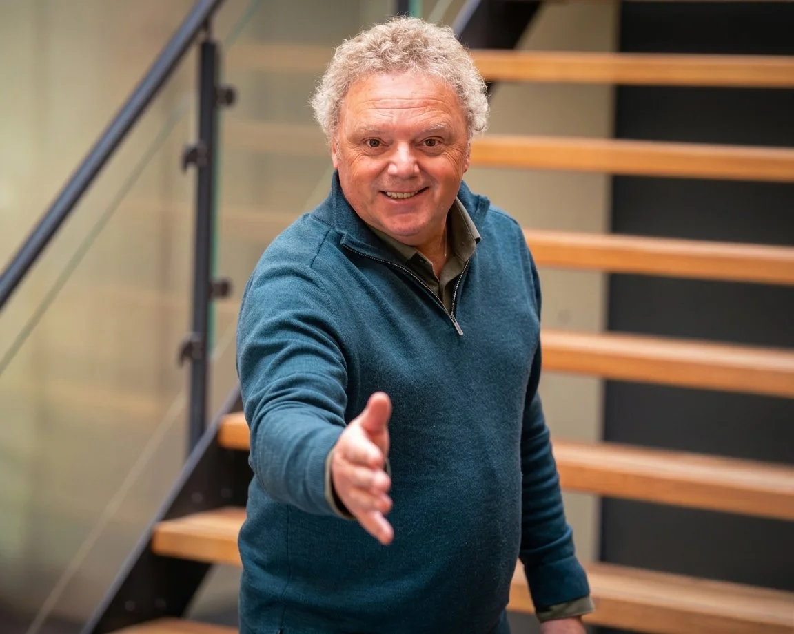 A smiling man with curly gray hair shaking hands with people on a wooden staircase