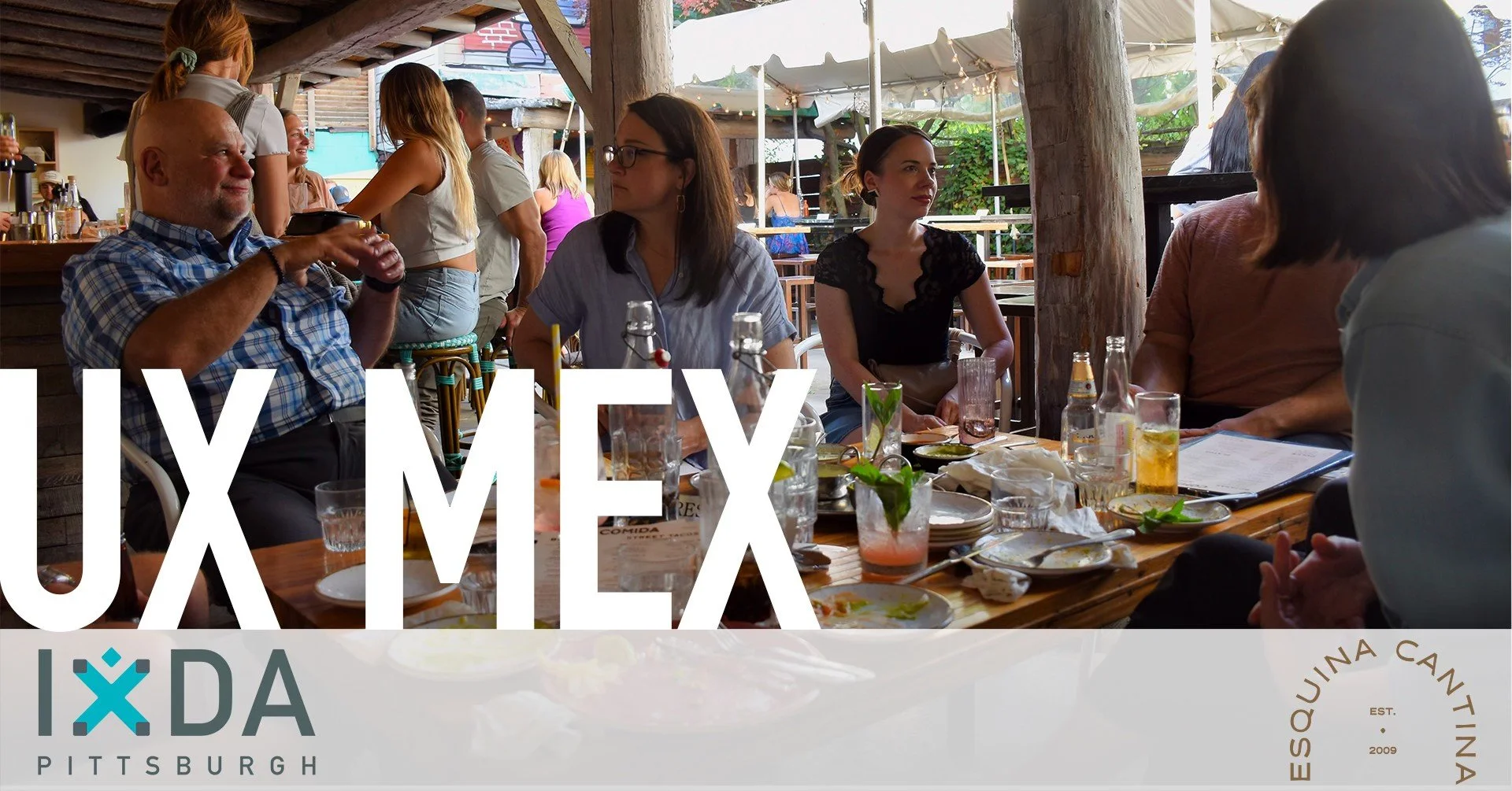 People seated and conversing around an outdoor table covered in dinnerware and drink glasses.