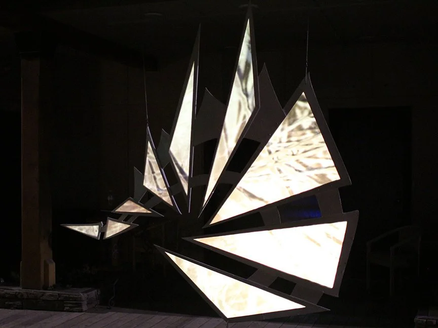 A hanging triangular sculpture with golden projected light