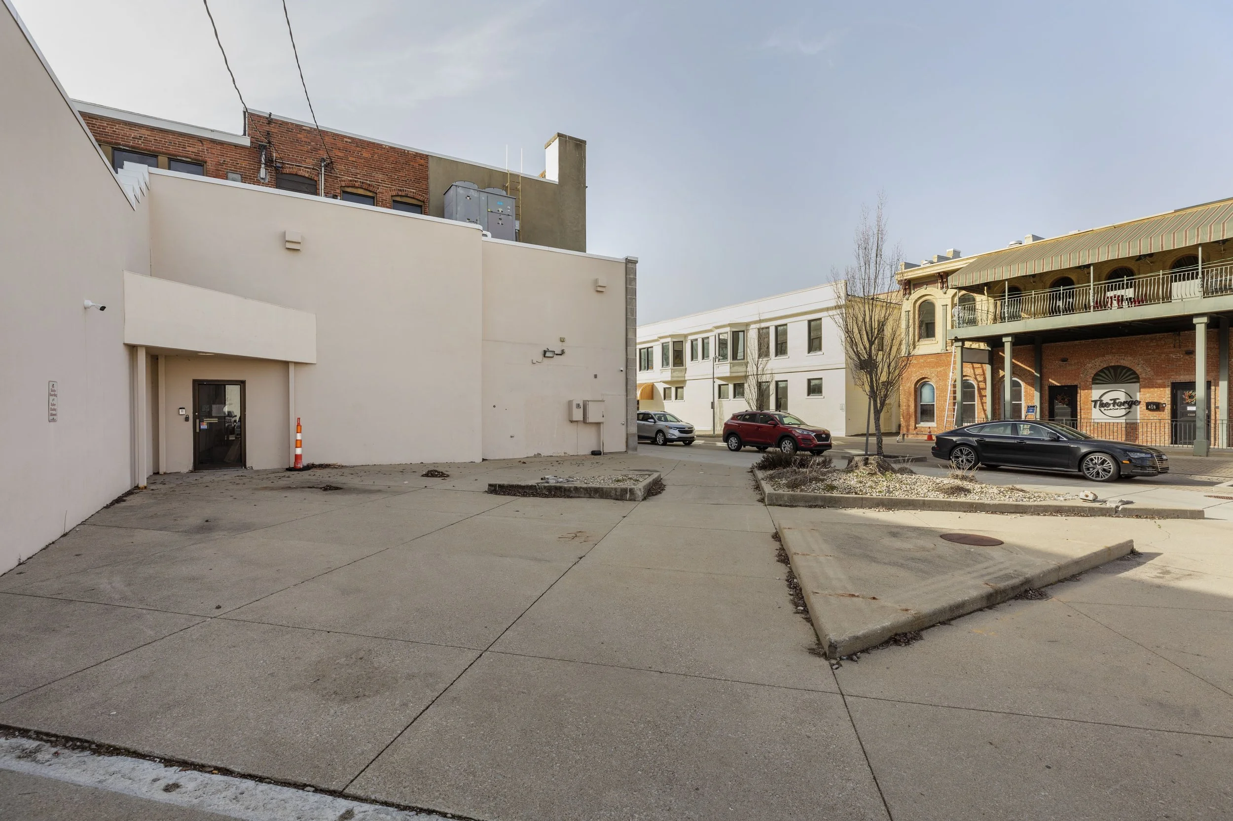 Empty parking lot with a small construction cone, surrounded by buildings and parked cars on a clear day.