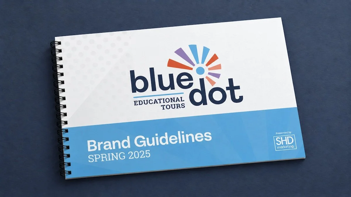 Spiral-bound booklet titled "Blue Dot Educational Tours Brand Guidelines Spring 2025" with the Blue Dot logo and a colorful graphic at the top, and a small SHD marketing logo at the bottom right corner.