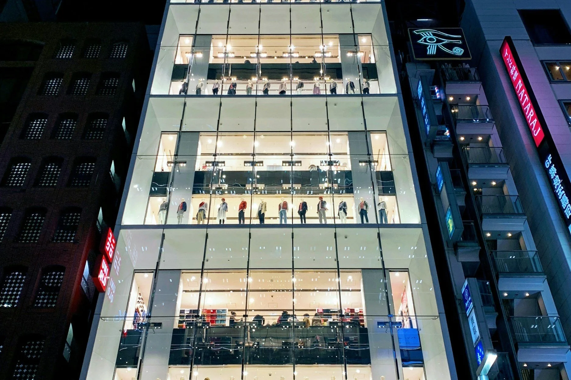 Illuminated multi-story clothing store with mannequins and glass facade at night.