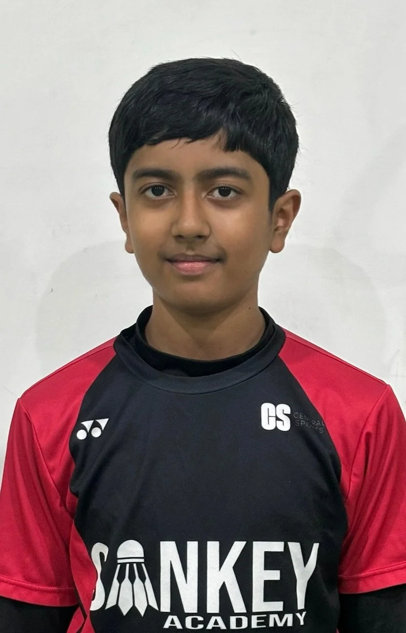 A young boy wearing a black and red sports jersey standing against a plain white wall.