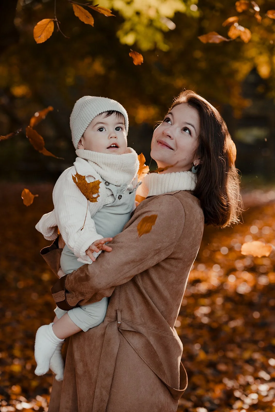 une femme tenant un jeune garçon dans un parc pendant l'automne, des feuilles tombent autour d'eux